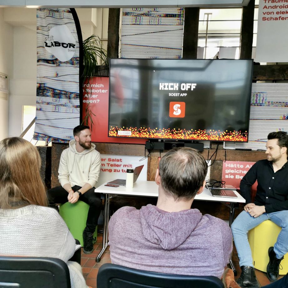 Eine Gruppe von Menschen sitzt im stadtLABOR Soest und schaut auf einen Bildschirm eine einer Präsentation zur SoestApp.