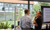 Zwei Mitarbeitende der Stadt stehen vor einer Präsentationswand und reden miteinander