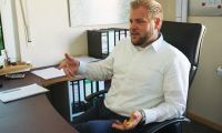 Porträtfoto von Lukas Brüggemann, der gestikulierend am Schreibtisch sitzt.