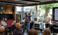 Menschen sitzen bei der Veranstaltung Klimaforum und hören einem Mann zu, der vorne steht und etwas präsentiert.