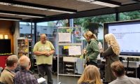 Menschen sitzen bei der Veranstaltung Klimaforum und hören einer Gruppe zu, die vorne steht und etwas präsentiert.