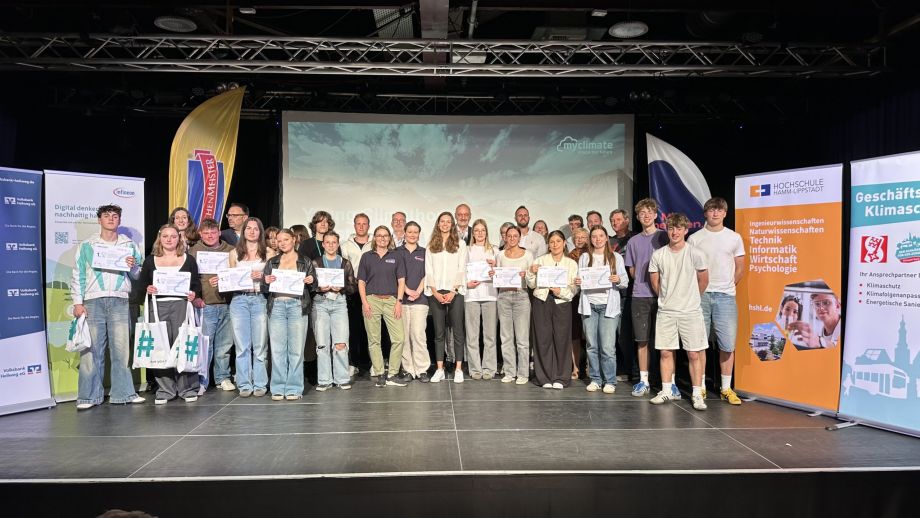 Das Bild zeigt eine große Gruppe von Menschen auf einer Bühne, die alle an der Veranstaltung Young Climathon teilgenommen haben. Alle Blicken in die Kamera und die Schülerinnen und Schüler aus den Gewinnergruppen präsentieren ihr Urkunden.