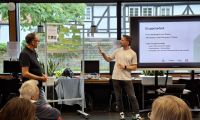 Menschen sitzen bei der Veranstaltung Klimaforum und hören zwei Mitarbeitenden der Stadt zu, die vorne stehen und etwas präsentieren.