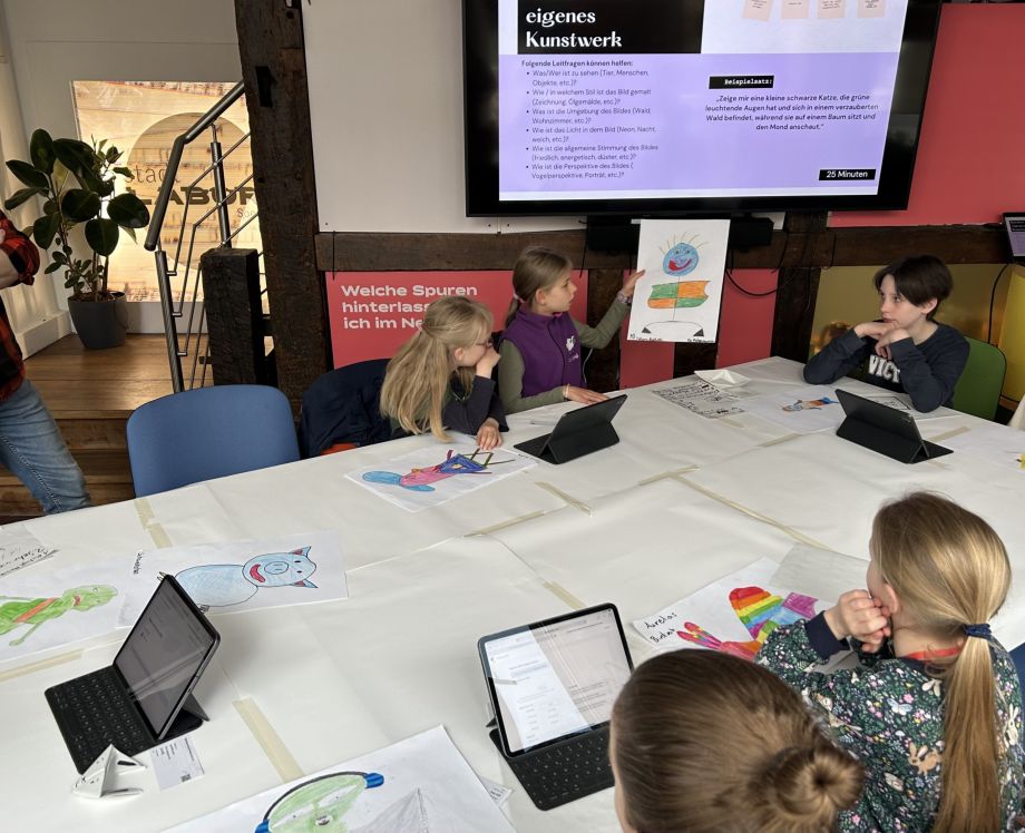 Kinder sitzen an einem Tisch und haben gemalte Bilder vor sich