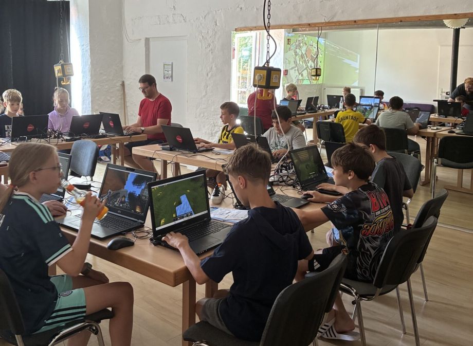 Das Bild zeigt eine Gruppe von Jugendlichen und Erwachsenen, die an Laptops Soest in Minecraft weiterbauen.