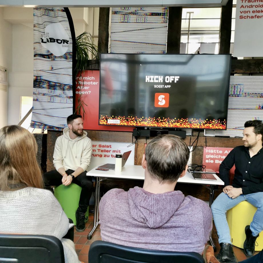 Eine Gruppe von Menschen sitzt im stadtLABOR Soest und schaut auf einen Bildschirm eine einer Präsentation zur SoestApp.