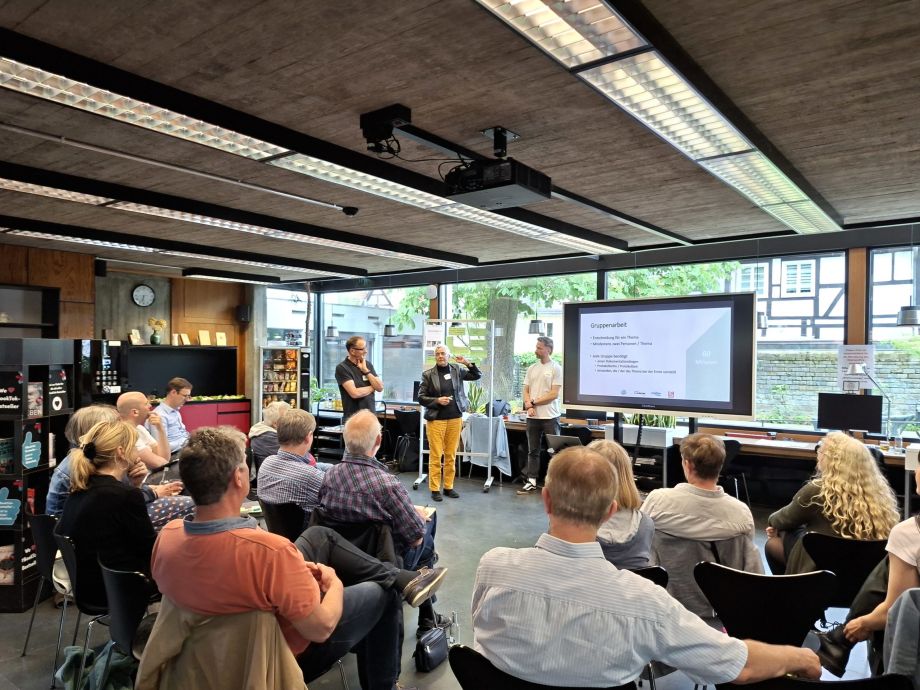 Menschen sitzen bei der Veranstaltung Klimaforum und hören einer Frau zu, die vorne steht und etwas präsentiert.