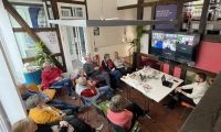Das Bild zeigt eine Gruppe von älteren Menschen im stadtLABOR Soest, die interessiert einem Online-Vortrag zuhören.