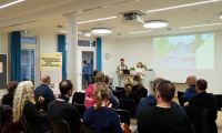 Ein Seminarraum, in dem vor einem Publikum von 20 Personen zwei Vortragenden die Abendveranstaltung Klimaforum moderieren. Im Hintergrund ist eine Popwerpoint-Präsentation an der Wand zu sehen. Die Vortragenden gestikulieren und Blicken in die Menge.