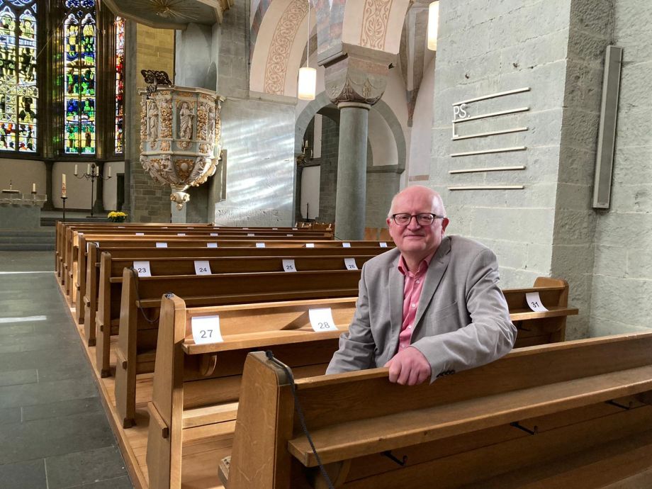 Porträtfoto von Heiner Roger, der auf einer Kirchenbank sitzt.