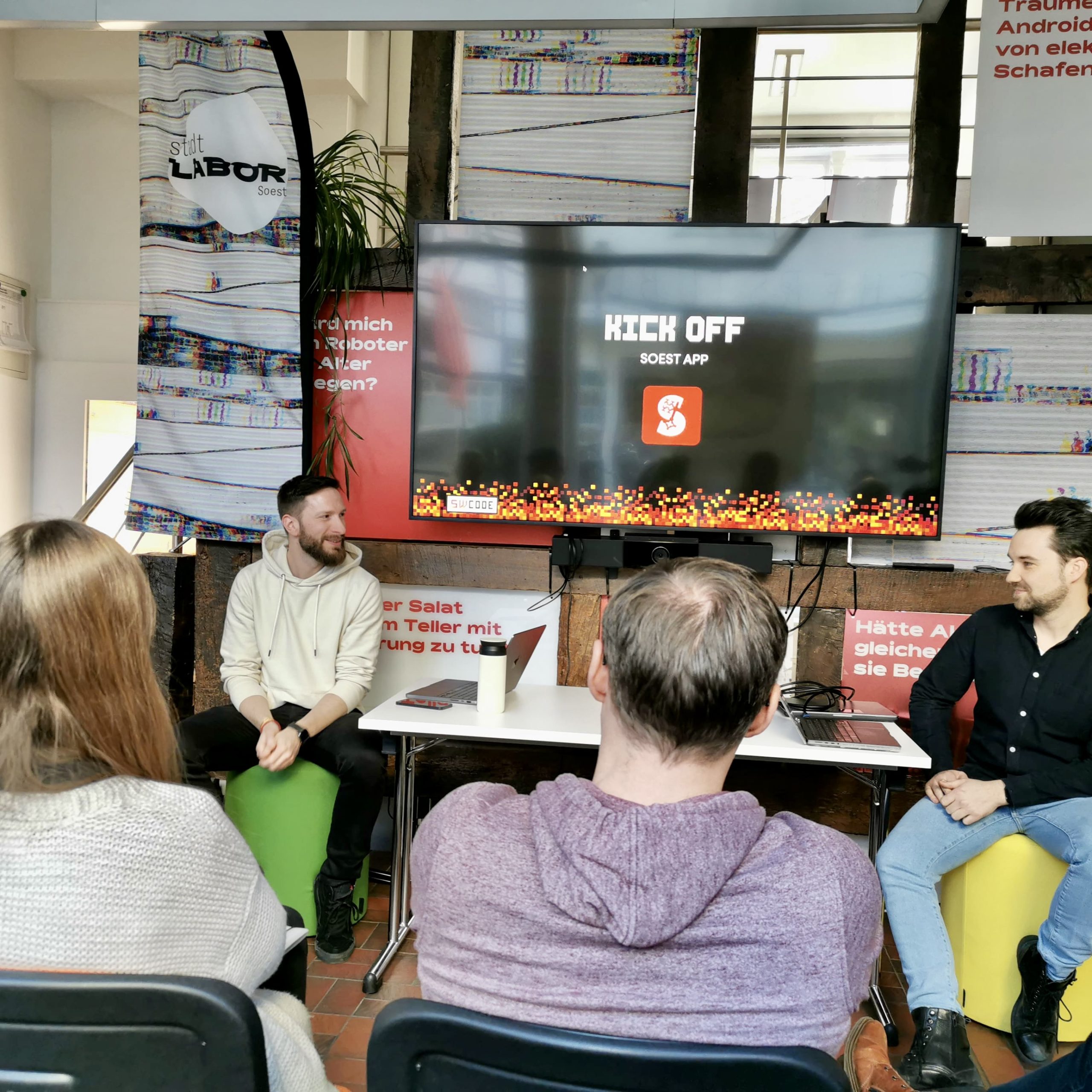 Eine Gruppe von Menschen sitzt im stadtLABOR Soest und schaut auf einen Bildschirm eine einer Präsentation zur SoestApp.