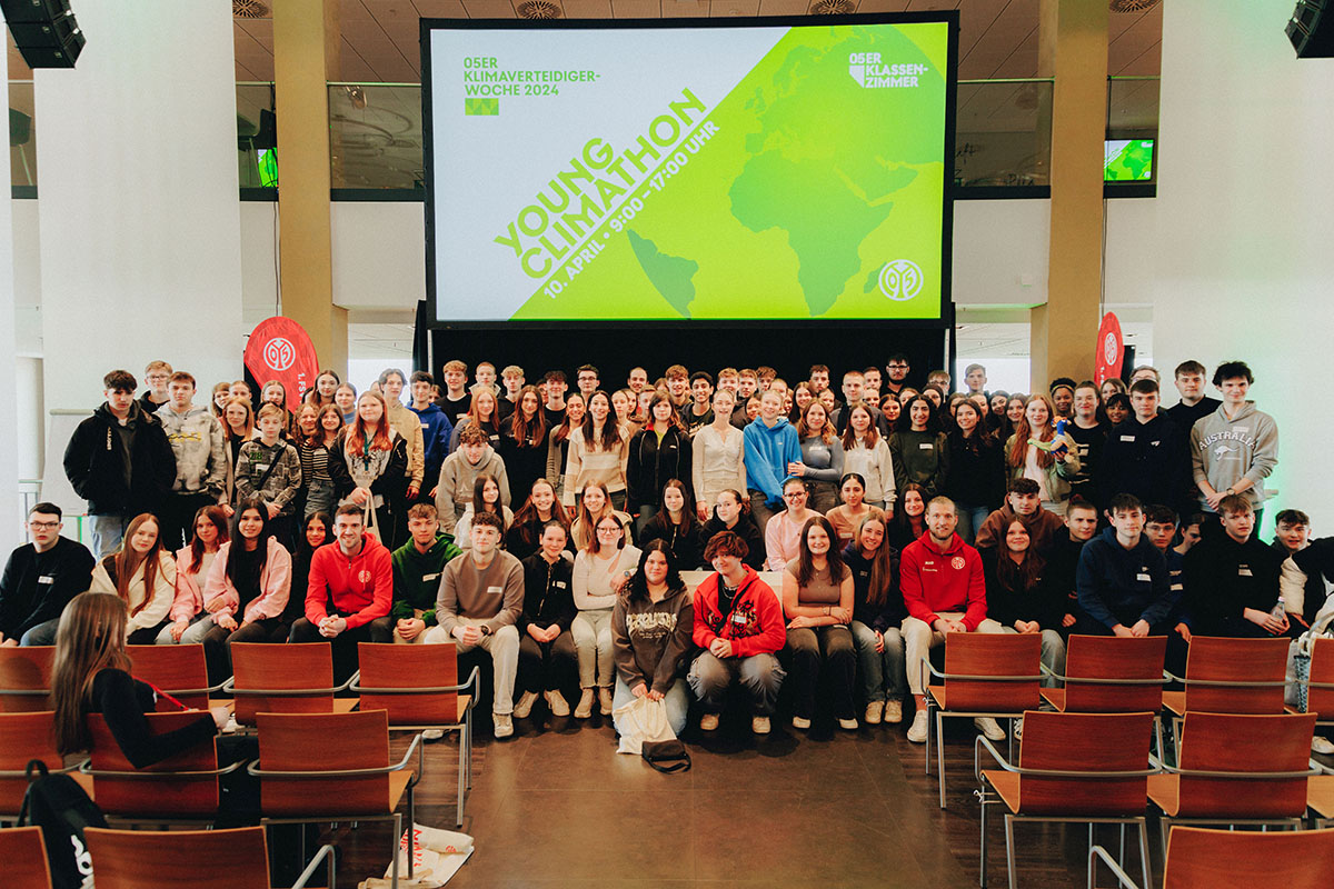 Ein Gruppenbild von einer Schulgruppe, im Hintergrund ist eine große Leinwand zu sehen mit dem Logo des Young Climathon