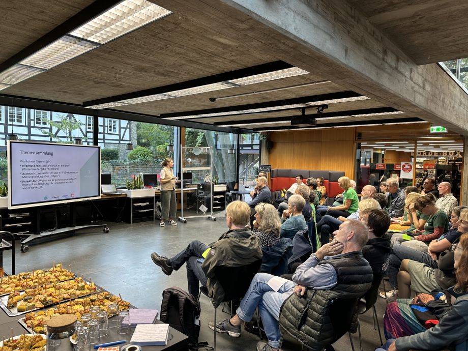 Menschen sitzen bei der Veranstaltung Klimaforum in der Stadtbücherei, eine Frau steht vorne und erklärt etwas
