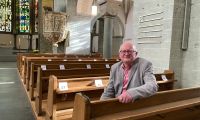 Porträtfoto von Heiner Roger, der auf einer Kirchenbank sitzt.