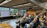 Menschen sitzen bei der Veranstaltung Klimaforum in der Stadtbücherei, eine Frau steht vorne und erklärt etwas