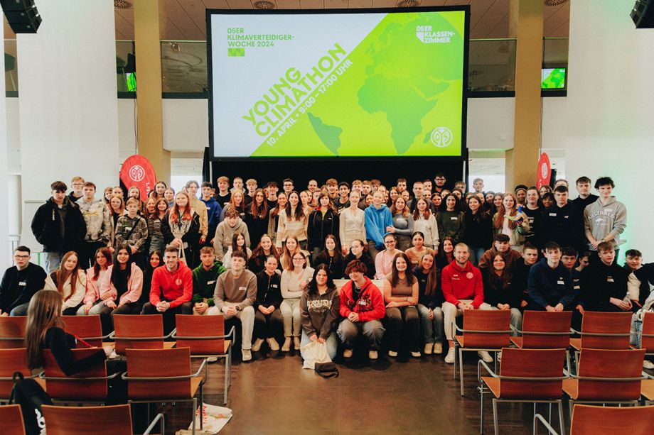 Ein Gruppenbild von einer Schulgruppe, im Hintergrund ist eine große Leinwand zu sehen mit dem Logo des Young Climathon