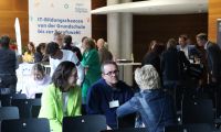 Menschen unterhalten sich an einem Tisch. Im Hintergrund sind weitere Personen zu sehen, die in Gespräche vertieft sind.