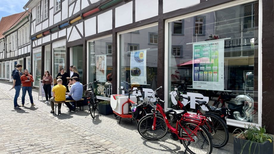 Eine Gruppe von Menschen steht vor dem sonnenbeschienen Stadtlabor und ist in Gespräche vertieft.