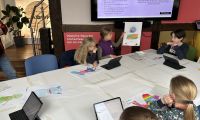 Kinder sitzen an einem Tisch und haben gemalte Bilder vor sich 